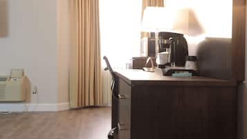 A hotel room with a desk, a coffee maker, a lamp, a telephone, and a window with curtains.