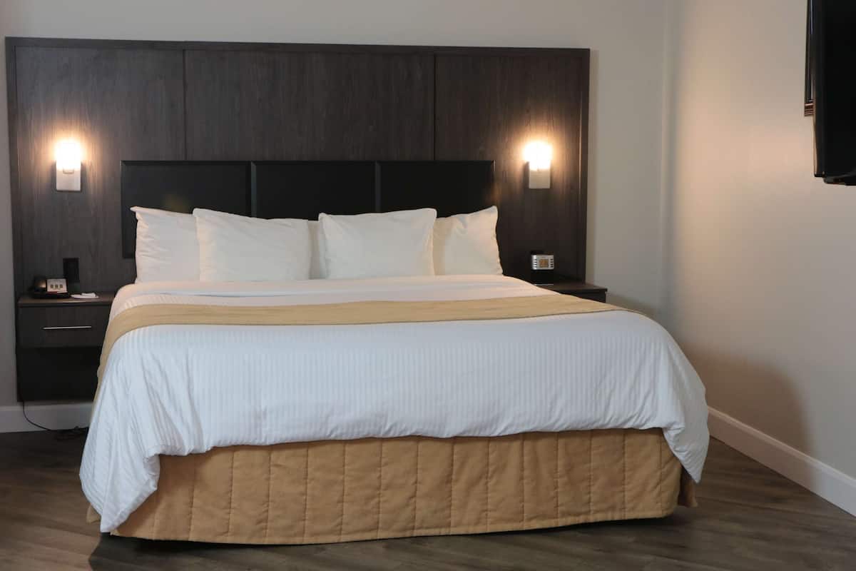 A neatly made bed with a dark headboard and two wall-mounted lights, a bedside table with a phone and a small lamp, and a wooden floor.