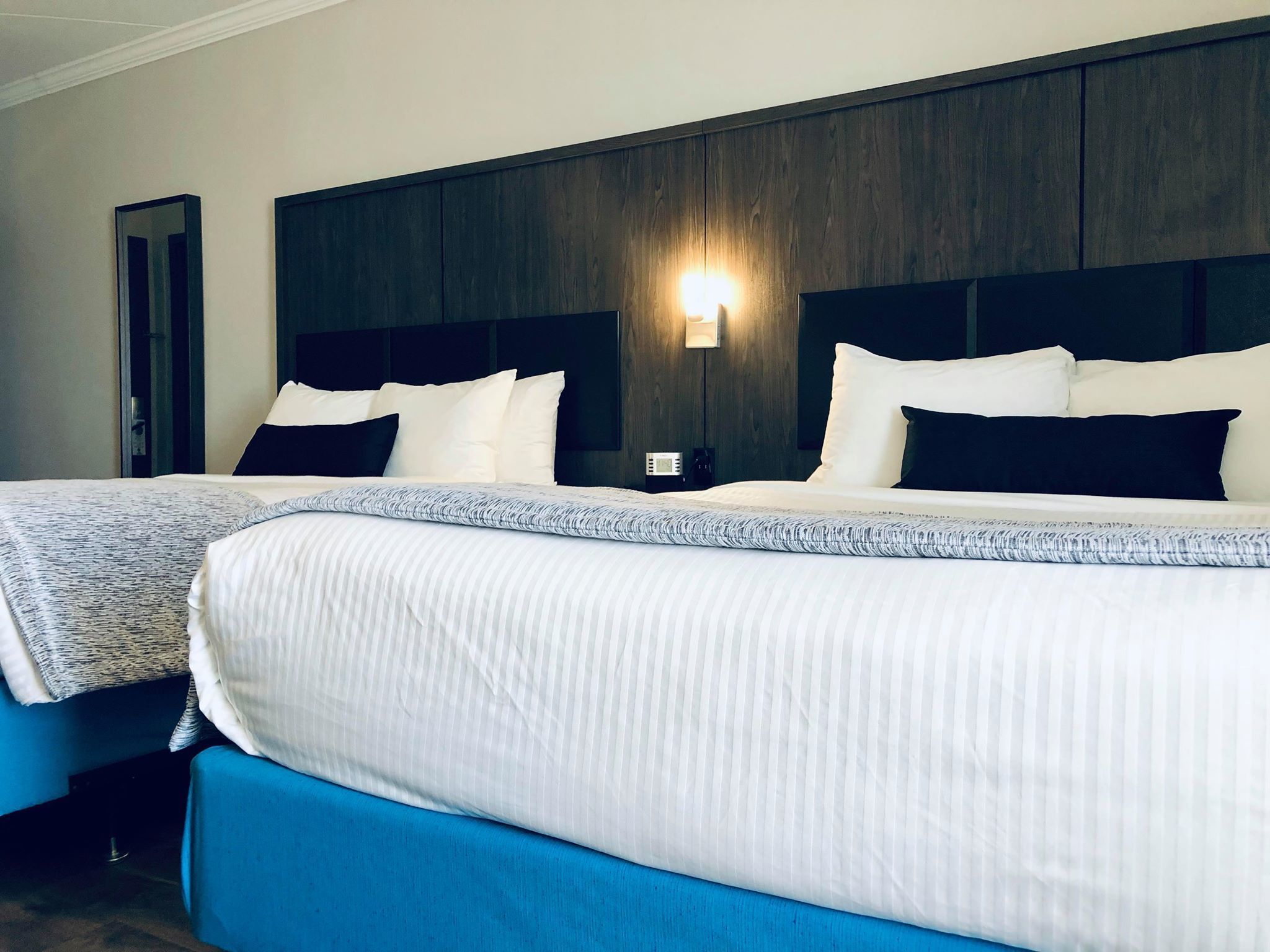 Een hotelkamer met twee bedden, donker houten hoofdeinden, witte beddengoed en een wandlamp.