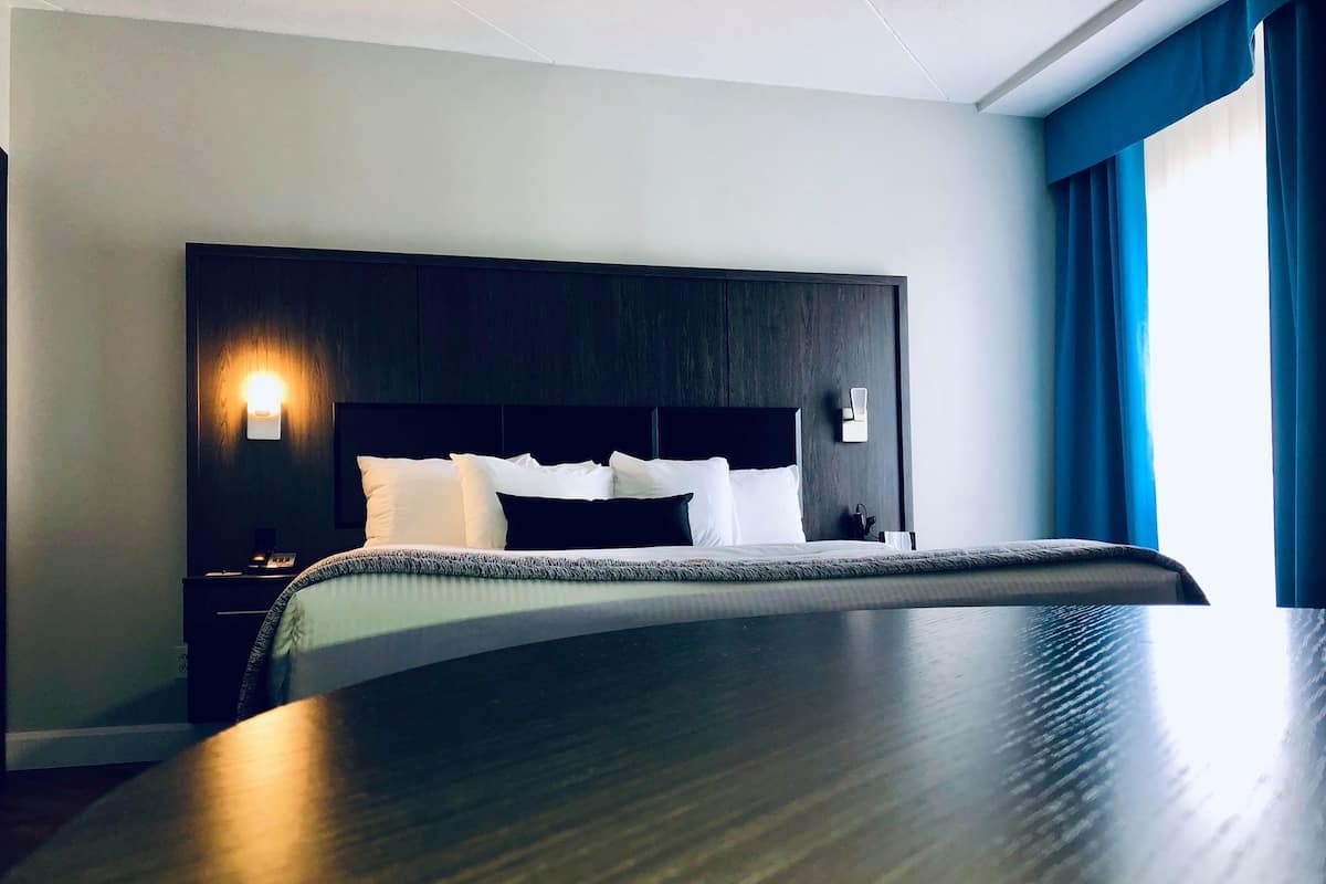 A hotel room with a large bed, dark headboard, bedside tables, and a wall-mounted lamp.