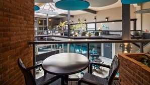 A modern indoor space with a glass railing, a round table, and chairs, overlooking a lower level with seating and plants. - Best Western Laval-Montreal (Laval)