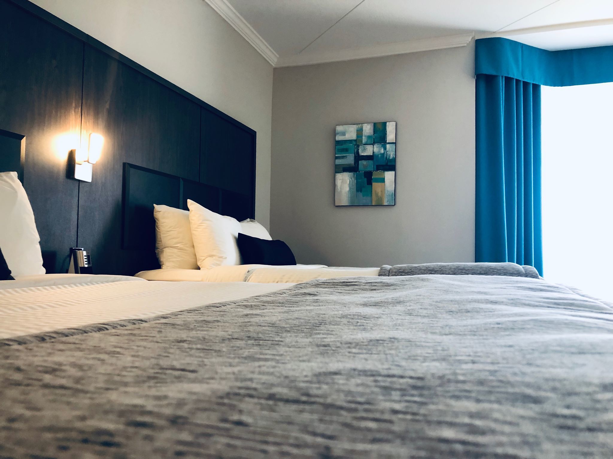 A hotel room with a large bed, a headboard, a wall-mounted artwork, and a window with curtains.
