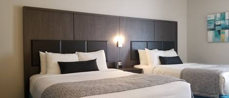 A hotel room with two beds, dark wood headboards, white bedding, and a wall-mounted light fixture.