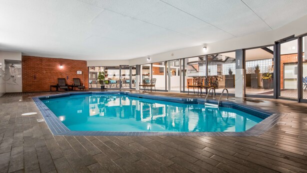 An indoor swimming pool with a wooden deck, a brick wall, and glass doors leading to an outdoor area. - Best Western Laval-Montreal (Laval)