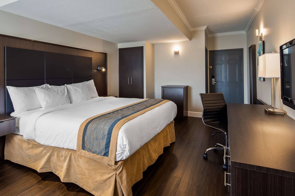 A hotel room with a bed, a desk, a chair, a TV, and a wardrobe.