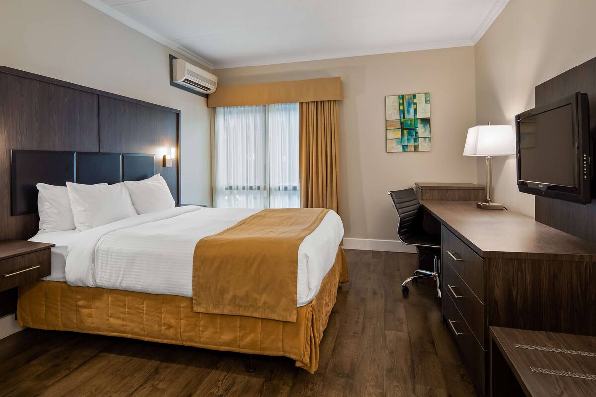 A hotel room with a bed, bedside tables, a desk, a chair, a television, and a window with curtains.