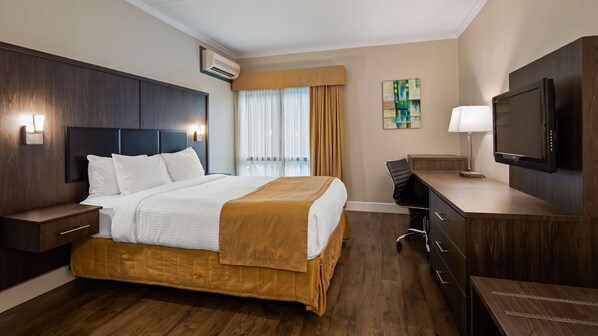 A hotel room with a bed, bedside tables, a desk, a chair, a television, and a window with curtains.