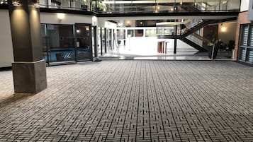 Un vaste atrium doté d’un sol à motifs, de plusieurs niveaux séparés par des rampes de verre et d’un escalier central.