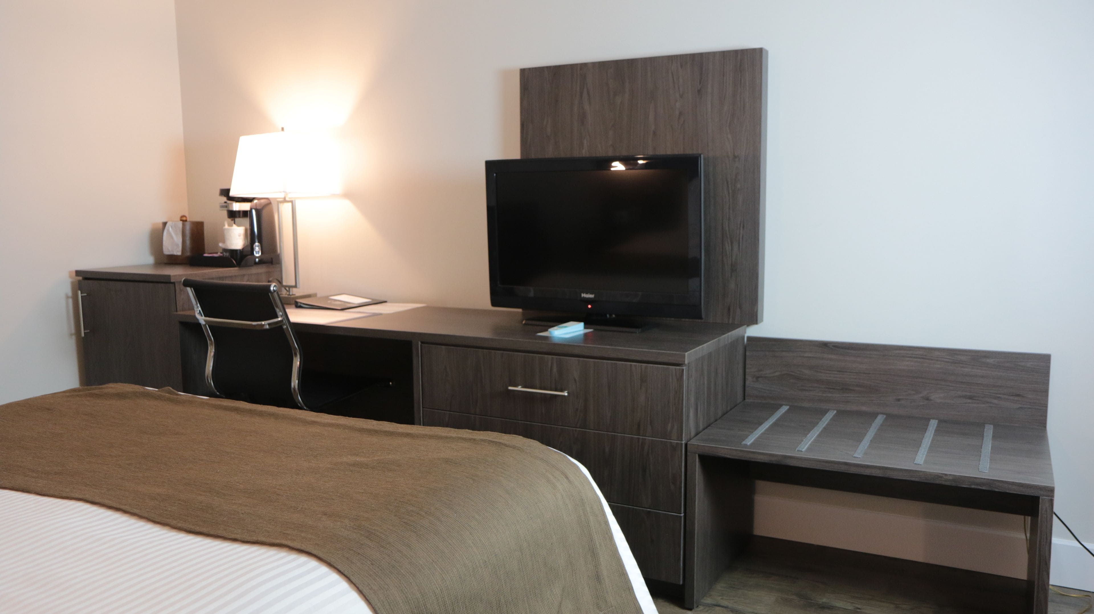 A hotel room with a bed, a desk with a chair, a television, and a lamp.