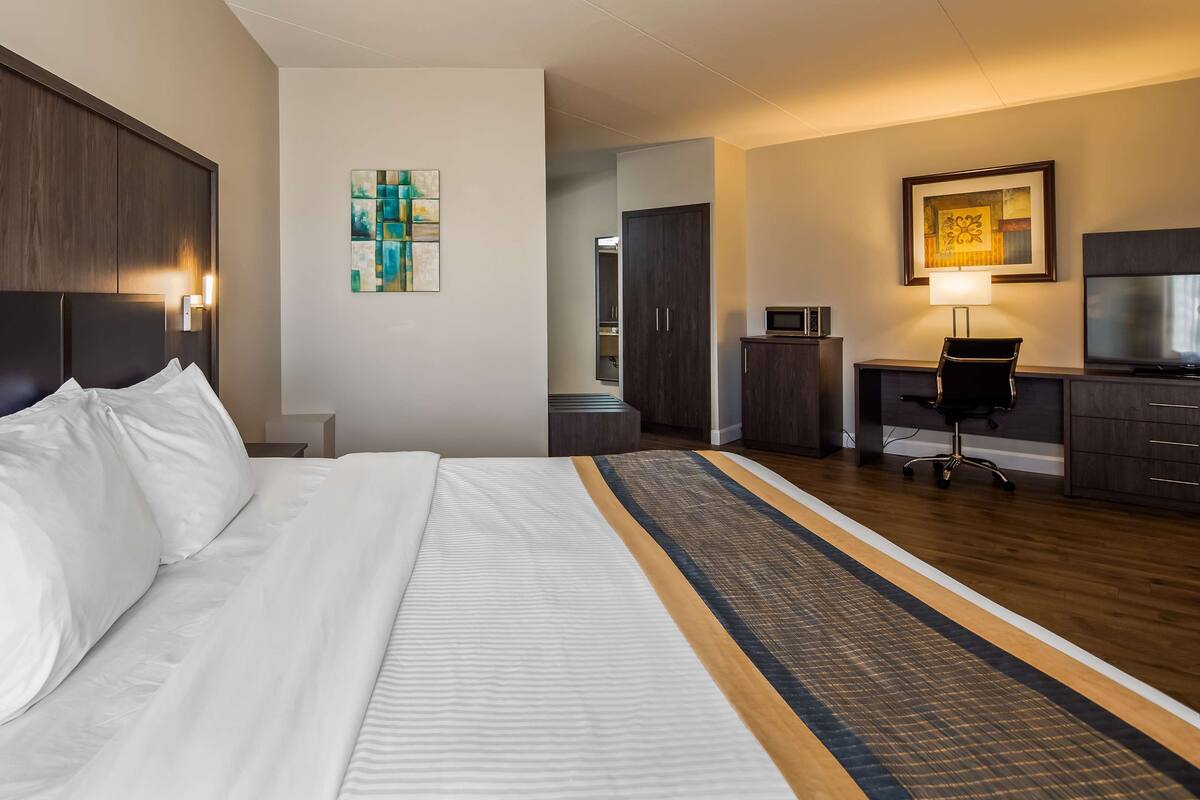 A hotel room with a large bed, a desk with a chair, a television, and a microwave.