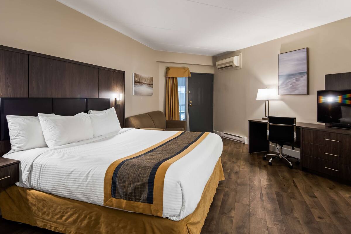 A hotel room with a large bed, a desk with a TV, a chair, and a lamp.