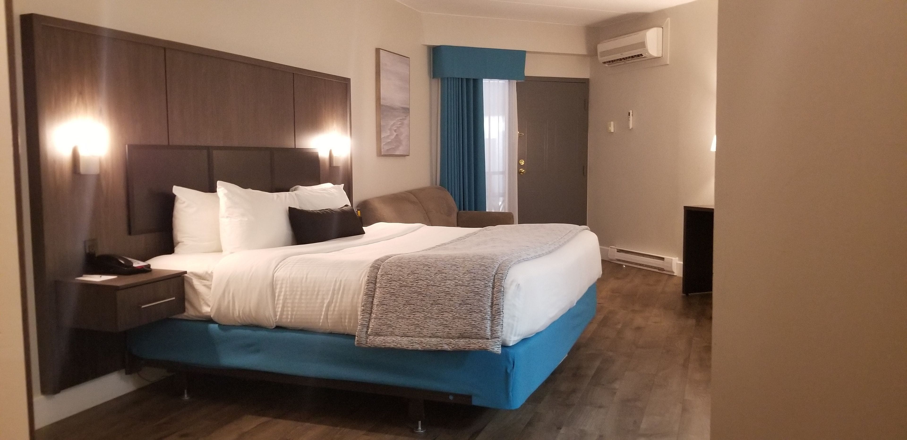 Een hotelkamer met een groot bed, nachtkastje, bureau en een airconditioning.