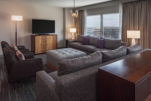 Una habitación de hotel moderna con un amplio sofá, un televisor de pantalla plana y vistas a la ciudad.