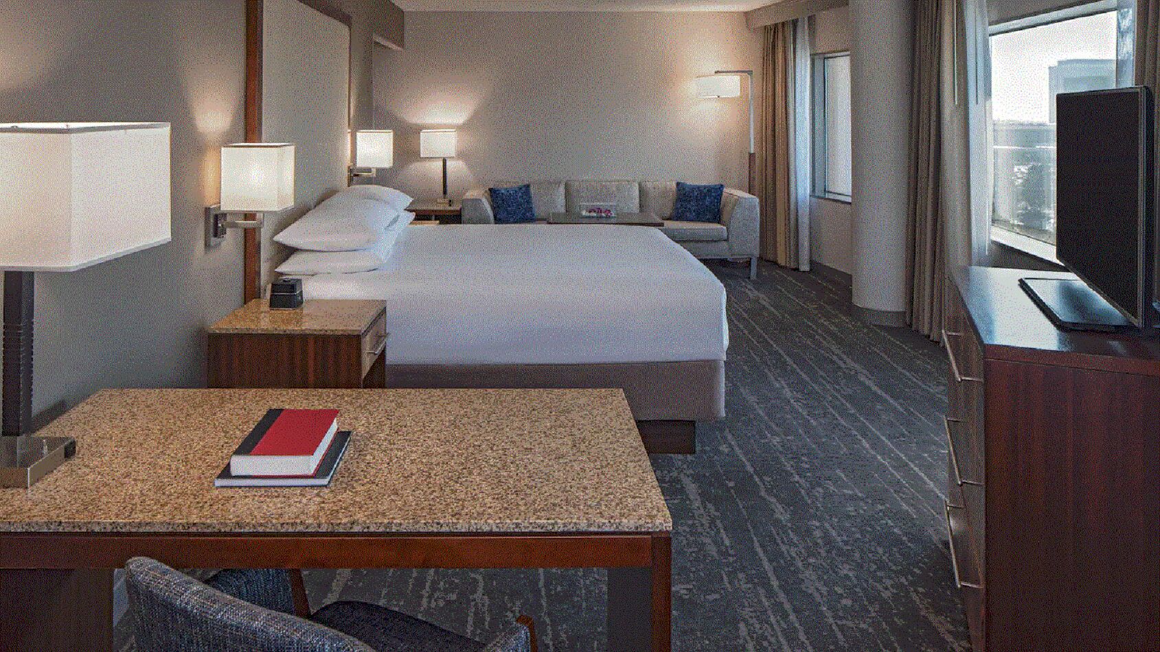 Ein Hotelzimmer mit Bett, Nachttischen, Schreibtisch, Stuhl und Fernseher.