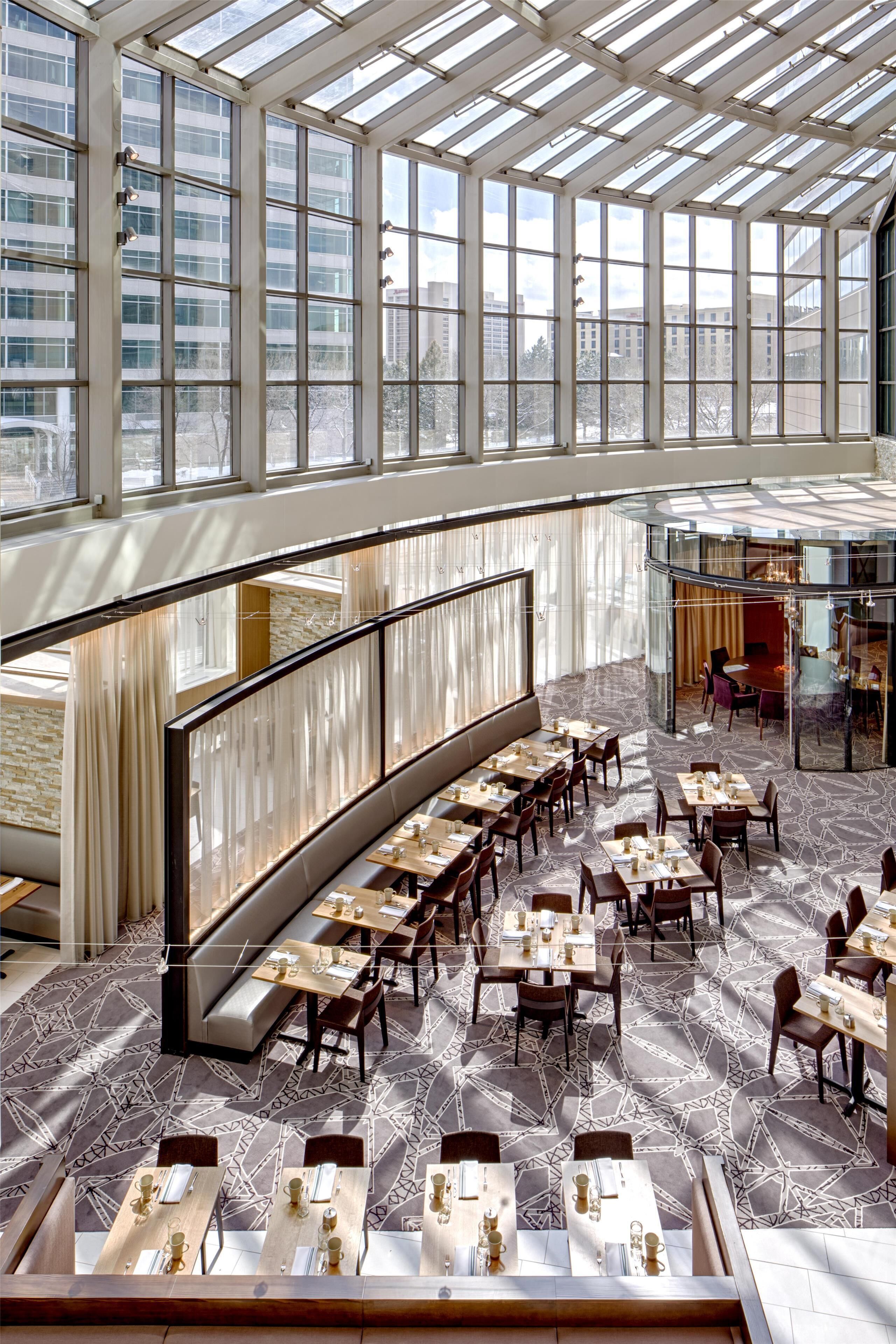 A spacious dining area with high ceilings and large windows, featuring a modern interior design with geometric patterned flooring and neatly arranged tables and chairs.