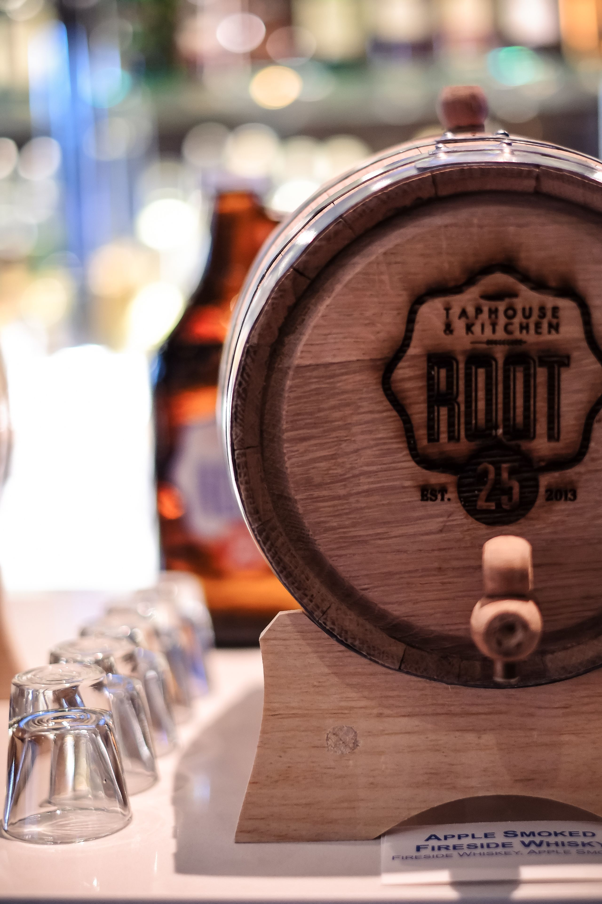 A taphouse & kitchen with a wooden barrel labeled "ROOT" and a sign for "Apple Smoked Fireside Whiskey".