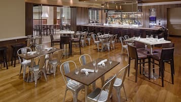 A spacious restaurant with multiple tables and chairs, a bar area, and a view of the cityscape.