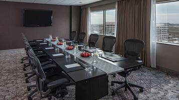 A conference room with a long table, chairs, a flat-screen TV, and a city view through large windows.