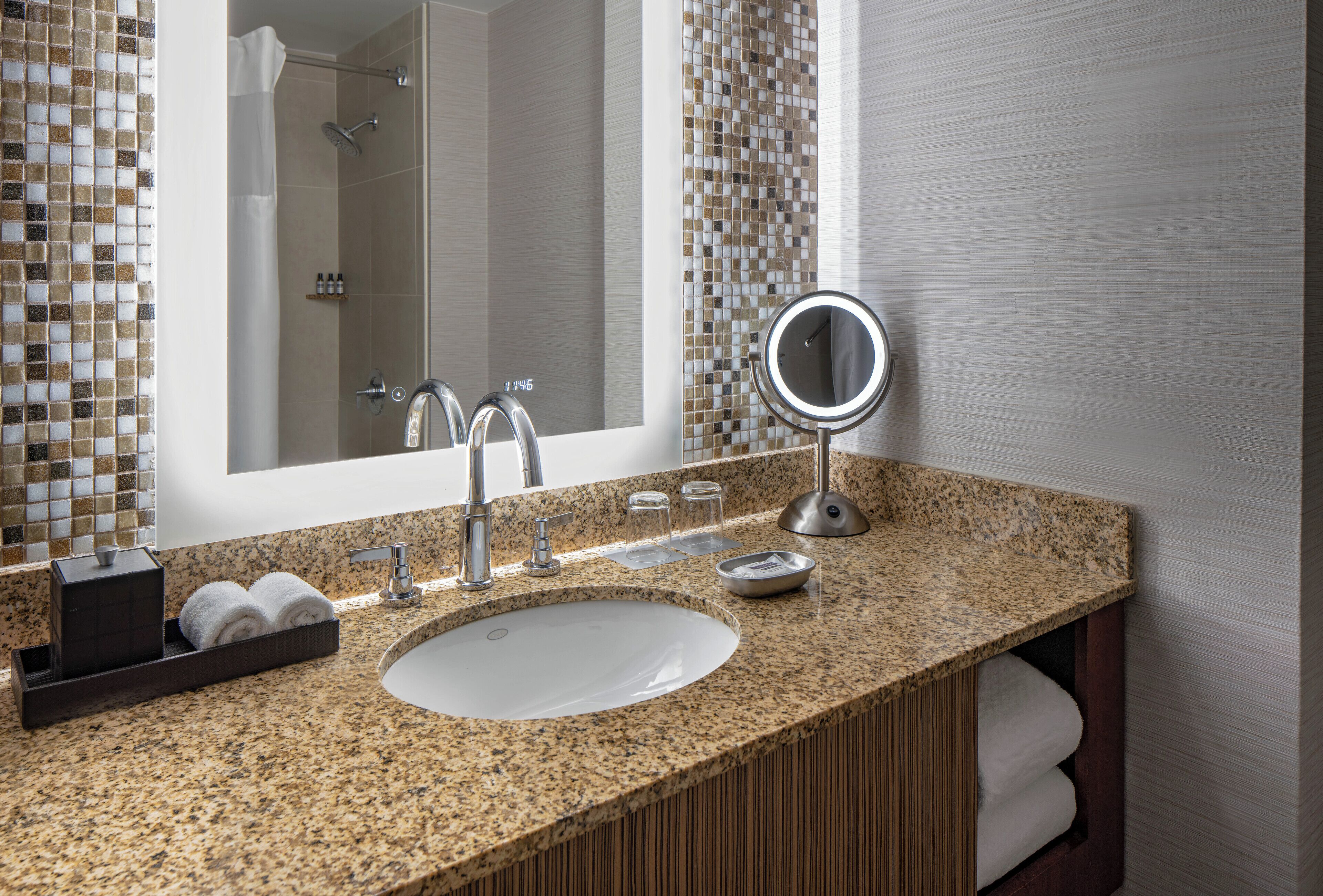 A bathroom with a granite countertop, a sink, a mirror, and a shower area.