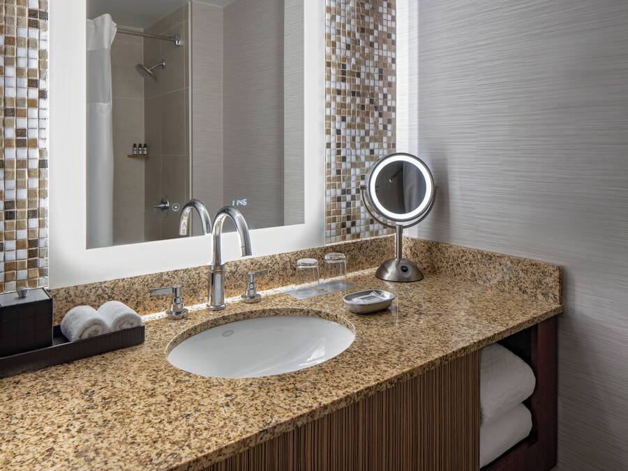 A bathroom with a granite countertop, a sink, a mirror, and a shower area.