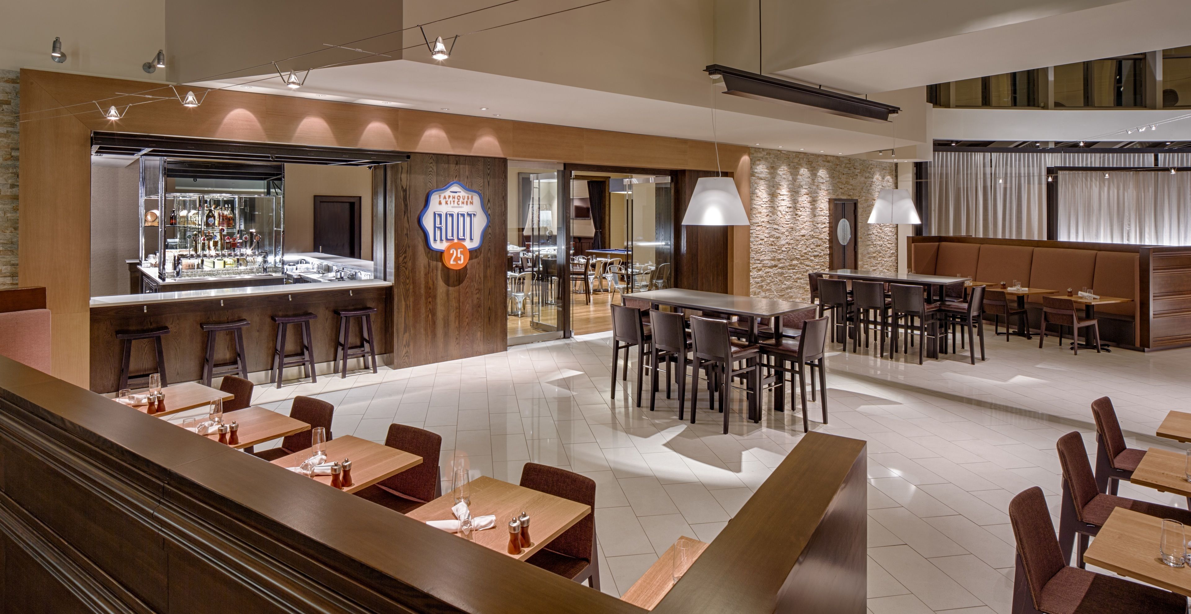 A modern restaurant with a bar area, multiple seating options including booths and tables, and a stone accent wall.