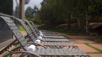 A row of metal lounge chairs with bottles on them, arranged on a paved walkway with a grassy area and trees in the background.