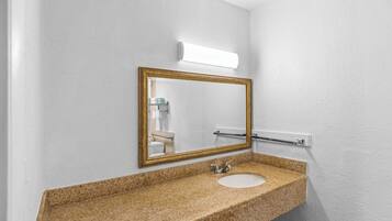 Un baño con encimera de granito, espejo con marco dorado, lavabo blanco y barra para toallas.