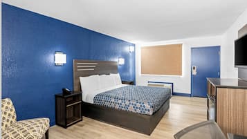 Una habitación de hotel con cama, mesita de noche, silla, escritorio, televisor y ventana con persianas.