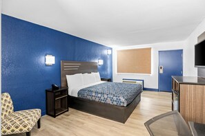 A hotel room with a bed, bedside table, chair, desk, TV, and a window with blinds. - Americas Best Value Inn Richmond South (Richmond)