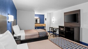 A hotel room with a bed, a desk, a television, and a bathroom visible in the background.