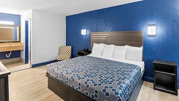 Ein Hotelzimmer mit einem großen Bett, einem Nachttisch, einem Spiegel und einem Badezimmer mit Waschbecken und Spiegel.