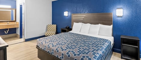 A hotel room with a large bed, a bedside table, a nightstand, a mirror, and a bathroom with a sink and mirror.