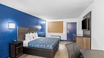 A hotel room with a bed, bedside table, chair, TV, and a wooden cabinet.