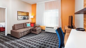 Hotelkamer met een bank, bureau, stoel, televisie en raam met gordijnen.