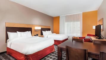 A hotel room with two beds, a dining table, and a TV.