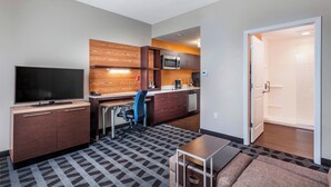 Een compacte hotelkamer met een kitchenette, een flatscreen televisie, een bank en een kamerbreed tapijt met dessin.