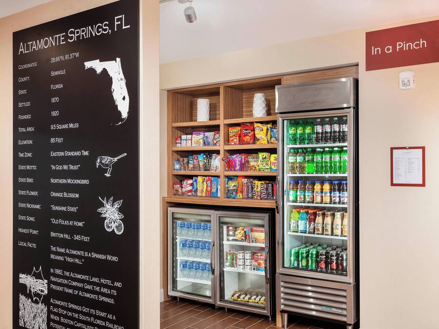 Une chambre d’hôtel dotée d’un tableau noir affichant des informations locales sur Altamonte Springs, en Floride, et d’un réfrigérateur rempli de boissons et d’en-cas.
