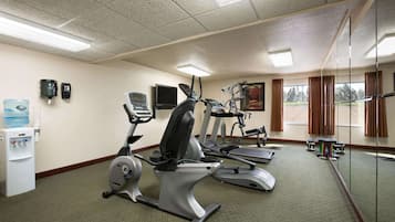Une salle de sport équipée de vélos d’appartement, de tapis de course et d’un distributeur d’eau.