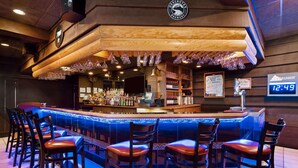 Un área de bar con mostrador de madera, taburetes y un reloj sobre el mostrador.