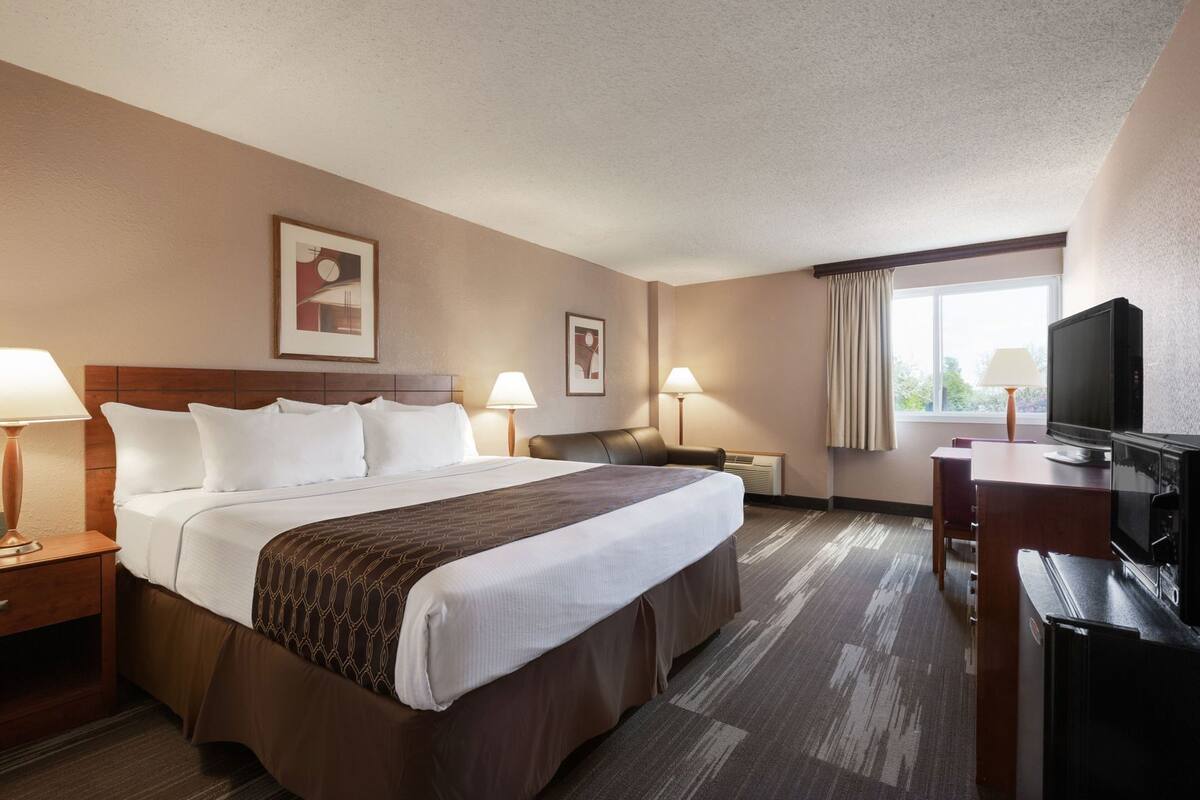 Una habitación de hotel con una cama grande, un escritorio con televisor y dos lámparas.