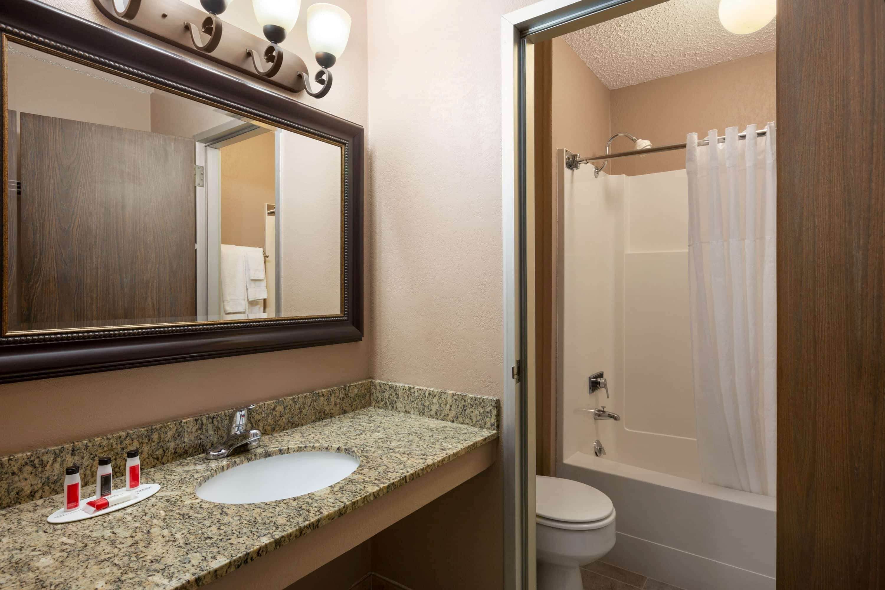 Un baño con lavamanos de encimera de granito, un espejo grande y una ducha con cortina.
