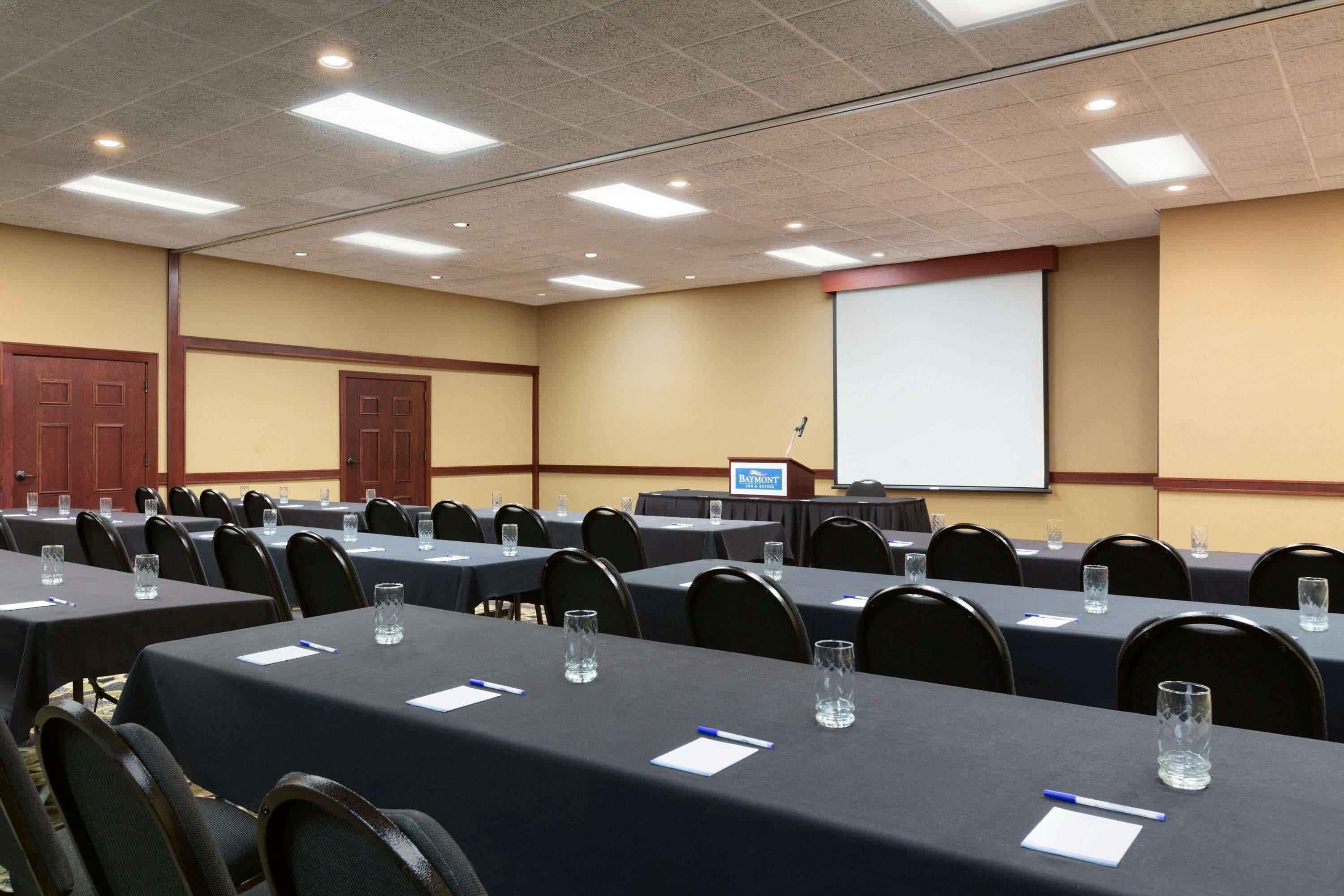 A conference room with multiple tables, chairs, a projector screen, and a podium.