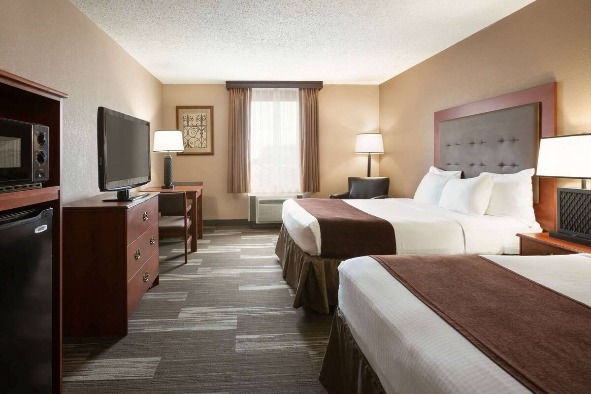 Una habitación de hotel con una cama, un escritorio con computadora, televisor y microondas.