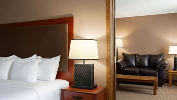 Une chambre d’hôtel avec un lit, une table de chevet avec une lampe, une petite table en bois, un canapé en cuir et un miroir qui reflète la pièce.