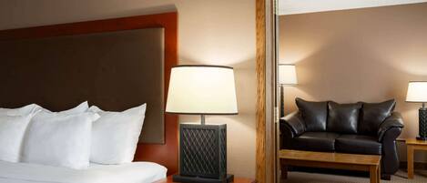 Une chambre d’hôtel avec un lit, une table de chevet avec une lampe, une petite table en bois, un canapé en cuir et un miroir qui reflète la pièce.