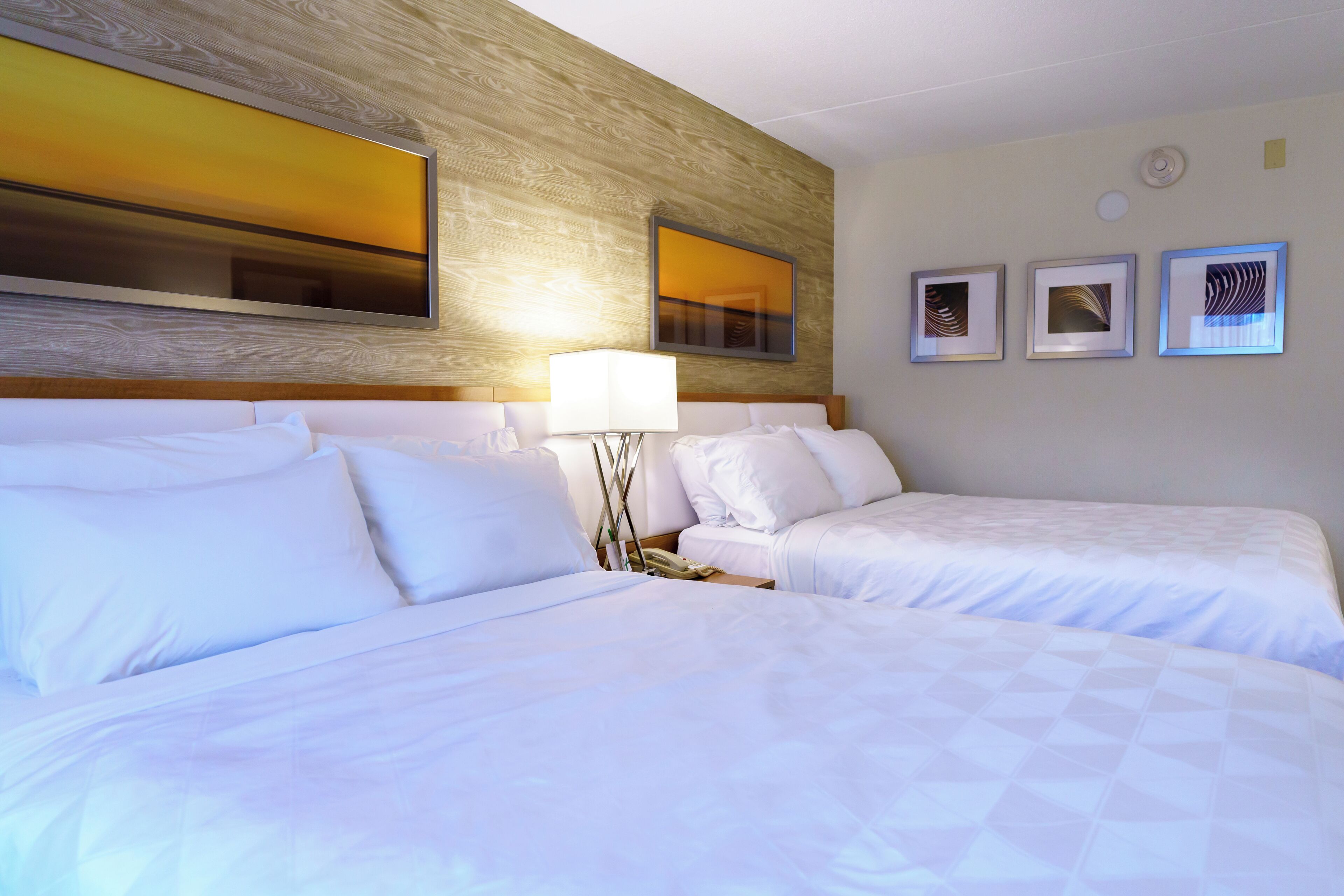 A hotel room with two beds, a wooden headboard, a large mirror, and three framed pictures on the wall.