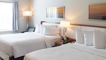 A hotel room with two beds, a nightstand with a lamp, a wall-mounted artwork, and a window with curtains.