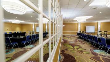 A conference room with a long table, blue chairs, a projector screen, and a patterned carpet.