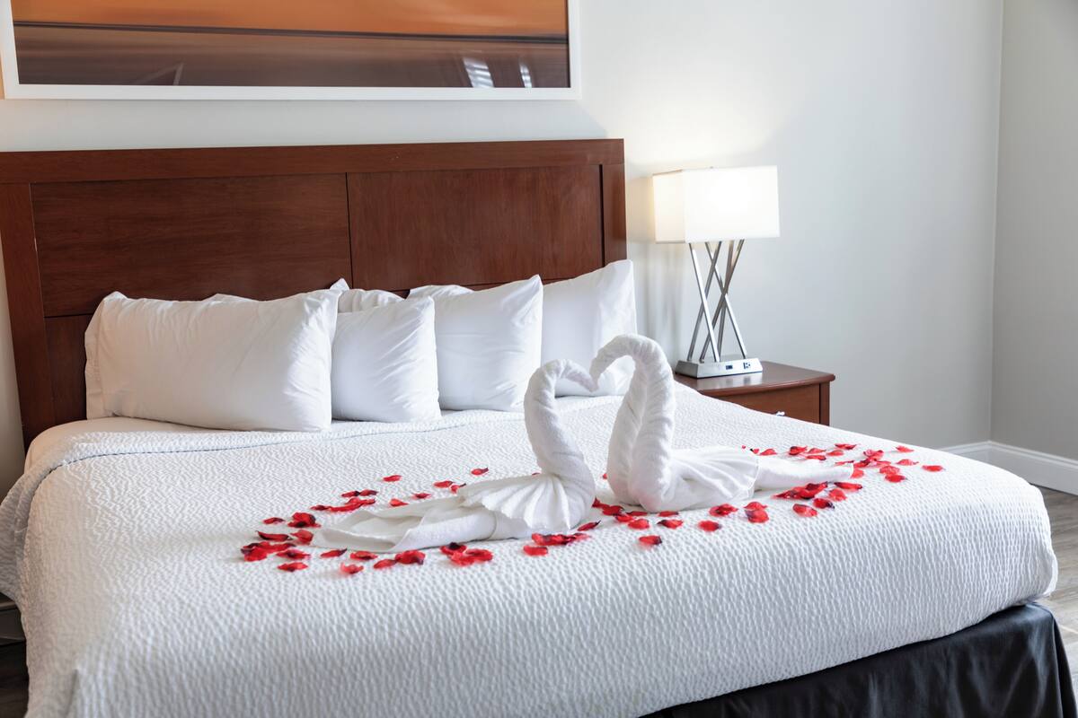 A neatly made bed with white linens, a wooden headboard, and a decorative swan made of towels on the bedspread.