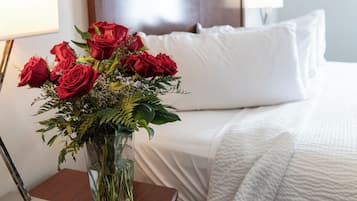 A hotel room with a bed, a bedside table with a lamp, and a vase of red roses.